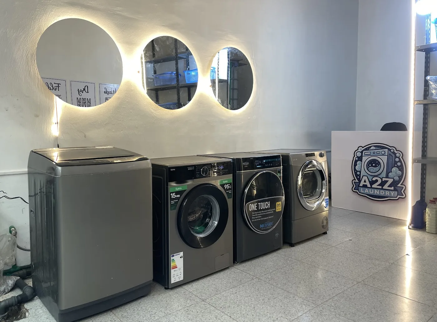 Inside A2Z Laundry: graphite front-loading washers under round backlit mirrors, with the A2Z sign